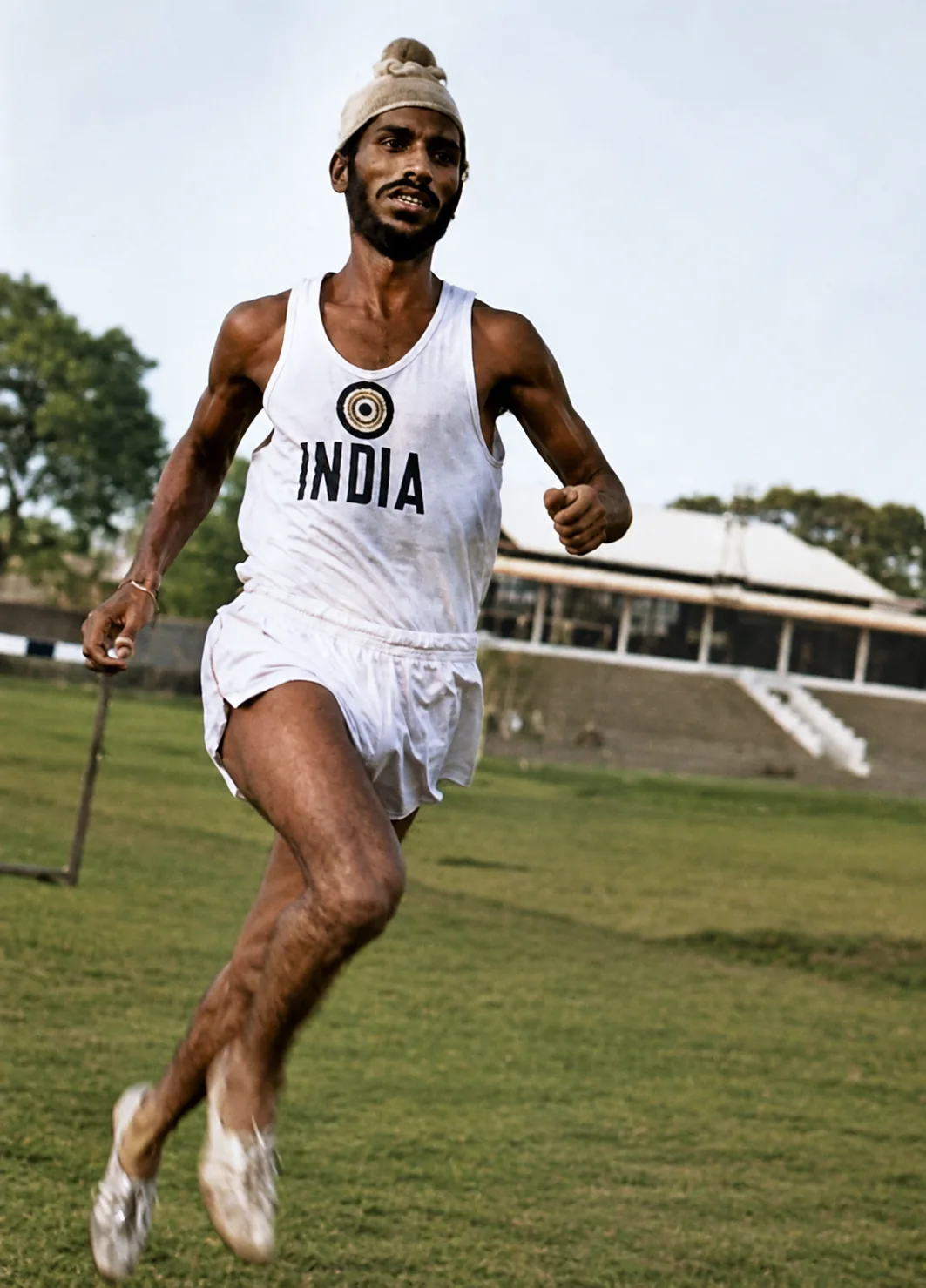 Illustration of Milkha Singh running across a grass field in an India vest and patka.